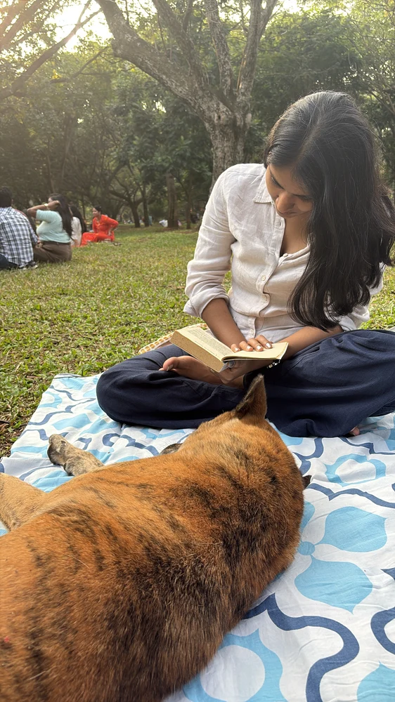 Kajal Jain reading a book at a park picnic, with a dog resting nearby