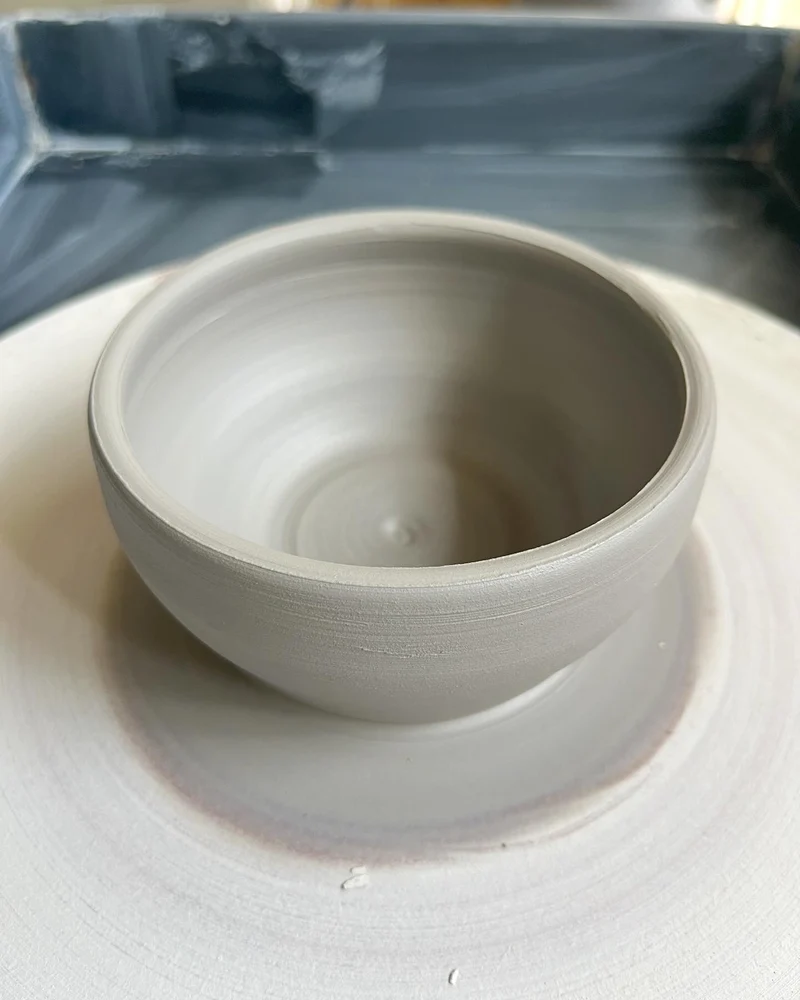 A hand-thrown ceramic bowl on a pottery wheel